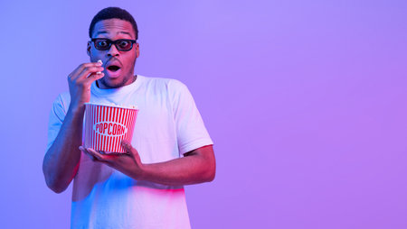 Young African Guy In 3D Glasses Eating Popcorn While Watching Scary Movieの写真素材