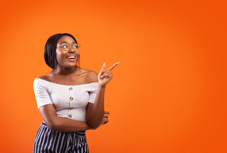 Happy African American Girl Pointing Finger Aside Standing, Orange Backgroundの写真素材