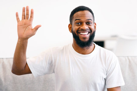 Cheerful African American Man Waving Hand Sitting On Couch Indoorの写真素材