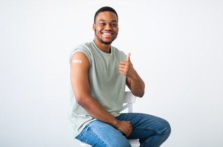 Cheerful Vaccinated Black Man Gesturing Thumbs-Up Approving Vaccination, White Backgroundの写真素材
