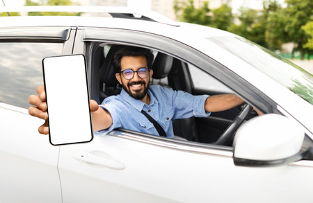 Smiling young eastern man sitting in auto, showing phoneの写真素材