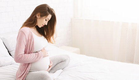 Pregnant Woman Sitting on Bed in Bright Bedroom During Daytime