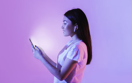 Woman with wireless headphones look at glowing smartphone