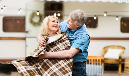 Happy senior man putting plaid on his beloved wifes shoulders at camping siteの写真素材