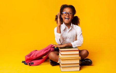 Nerdy Schoolgirl Raising Hand Sitting At Books Over Yellow Backgroundの写真素材