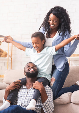 Black parents and little daughter having fun at home together.の写真素材