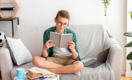 Intelligent teenager studying at home, reading book