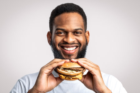 Cheerful African Man Holding Burger Smiling To Camera, White Backgroundの写真素材