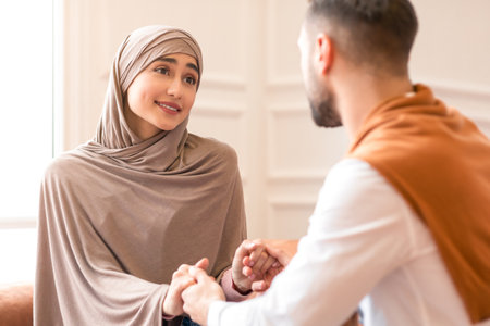 Modern Muslim Couple In Love Talking Holding Hands Sitting Indoorsの写真素材