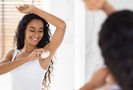 Beautiful Young Woman Applying Roller Deodorant To Armpit Zone In Bathroomの写真素材