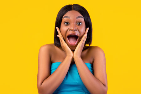 Excited African American woman in summer dress shouting in excitement, holding hands near face, orange backgroundの写真素材
