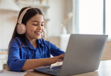 Schoolgirl Studying Online Typing On Laptop Wearing Earphones At Homeの写真素材