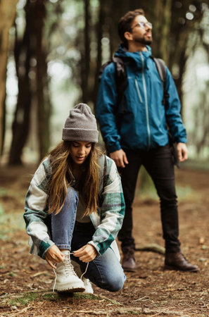 Smiling millennial caucasian guy and lady in jackets and backpacks travel in cold forest, tie...