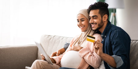Happy pregnant muslim couple shopping online with digital tablet and credit card