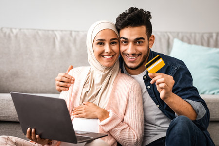 Joyful pregnant islamic couple using laptop and credit card for online shopingの写真素材