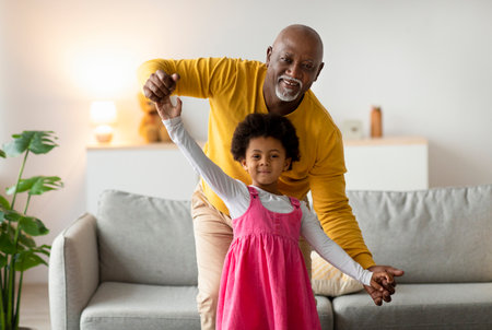 Smiling african american little girl and old man dancing and have funの写真素材