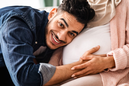 Future Father. Happy arab man listening his pregnant wifes belly, closeupの写真素材