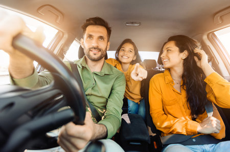 Joyful family moment in car, dad touching steering wheel, daughter pointsの写真素材