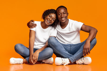 Carefree african couple sitting on floor and huggingの写真素材