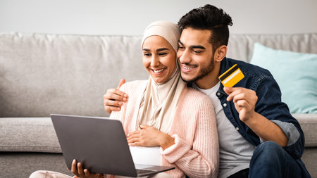 Expectant muslim couple shopping online with laptop and credit card at home