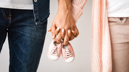 Closeup of pregnant couple carrying small baby shoes while holding hands togetherの写真素材
