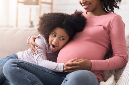 Excited little girl touching and listening to her pregnant mothers bellyの写真素材