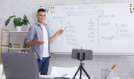 Modern gadgets for working remotely online at home during outbreak of covid-19. Smiling guy points to white board with English rules and looks at webcamの写真素材