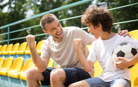 Dad and boy watching football game on stadium and cheeringの写真素材