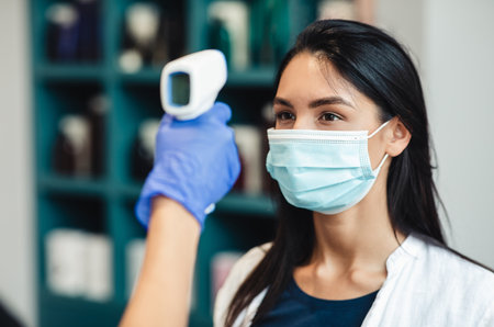 Young women getting body temperature control at enter of beauty salon