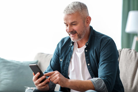 Smiling senior man using smartphone at home