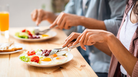 Unrecognizable couple using fork and knife while eating tasty breakfast in kitchenの写真素材