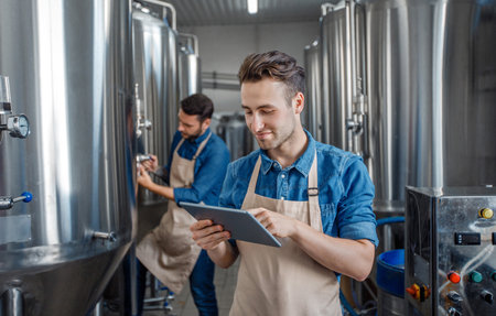 Quality control on brewery. Guys work near brewing kettles using tablet