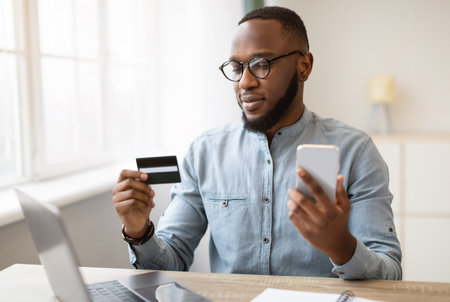 African American Businessman Using Cellphone And Credit Card In Officeの写真素材