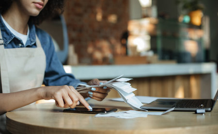 Busy african american lady owner in apron works with financial billsの写真素材