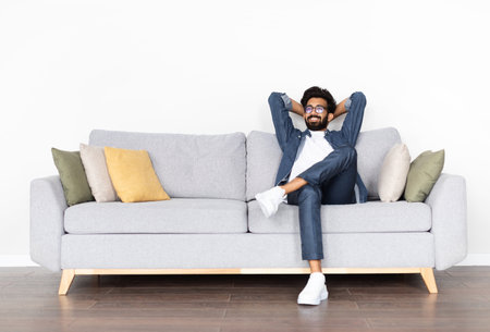 Relaxed happy young eastern guy chilling on couch at homeの写真素材