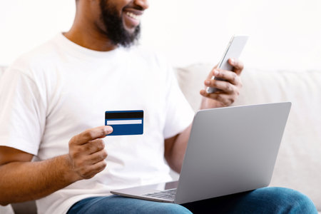 Black Man Using Phone And Credit Card Sitting At Homeの写真素材