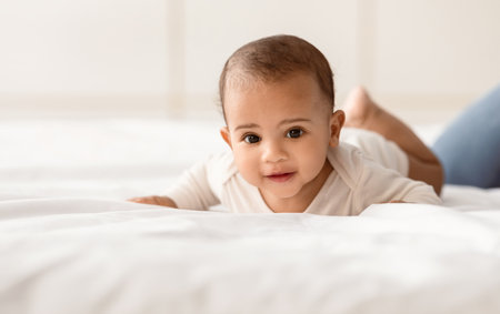 Cute little African American infant in bodysuit crawling on bed