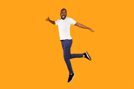 Shocked African American Guy Jumping Looking At Camera, Yellow Backgroundの写真素材
