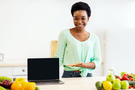 Black Woman Showing Laptop Screen Posing In Kitchen At Homeの写真素材