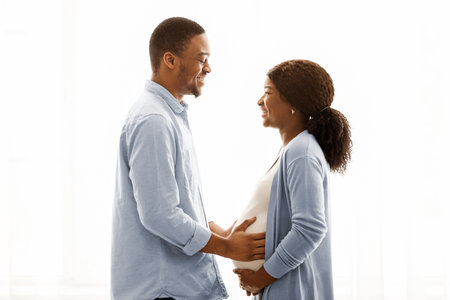 Loving pregnant black couple cuddling while spending time at homeの写真素材