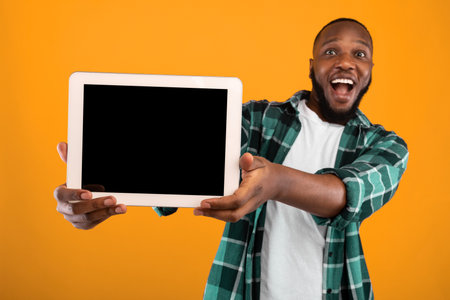 Excited Black Guy Showing Tablet Screen Posing Over Yellow Backgroundの写真素材