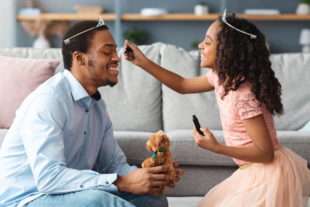 Excited little black girl putting make up on her father faceの写真素材