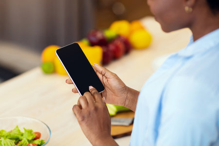African Lady Using Phone With Empty Screen In Kitchen, Croppedの写真素材