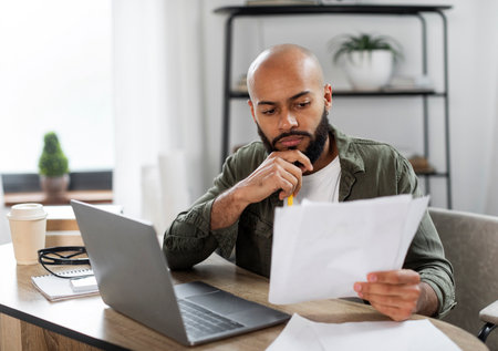 Serious male entrepreneur checking documents, reading financial reports while sitting at desk at...