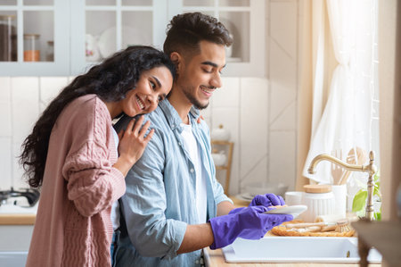 Young Arab Husband Washing Dishes After Lunch, Helping Wife With Domestic Choresの写真素材