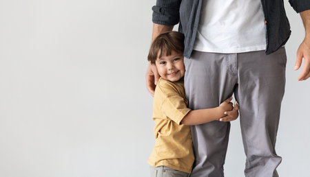 Happy little boy embracing his daddy, smiling to camera, feeling loved and safe, posing over grey wall with empty spaceの写真素材