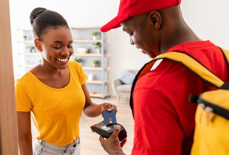 Cheerful Female Paying Deliveryman With Credit Card Standing At Homeの写真素材