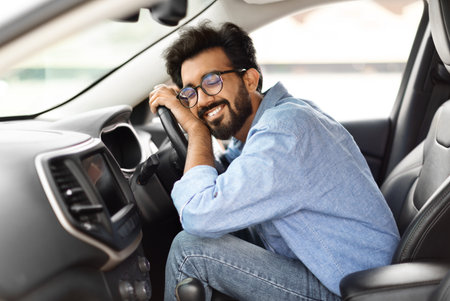 Thrilled young indian guy hugging steering wheel of new carの写真素材