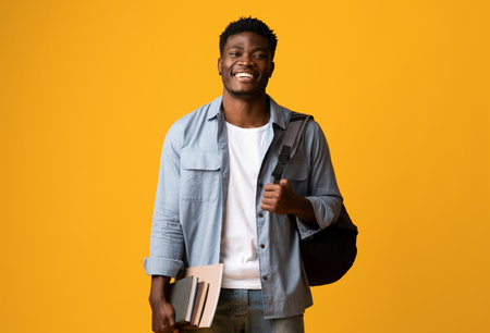 Positive millennial black man student with books on yellowの写真素材