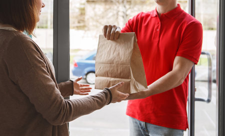Delivery with courier at home. Deliveryman gives paper package to girl client